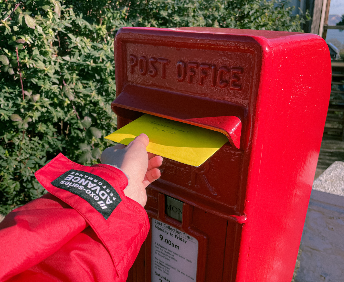 Postal service person posting a letter into a red postbox
